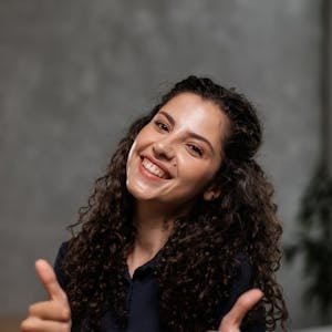 Cheerful woman with curly hair giving thumbs up indoors, smiling brightly.